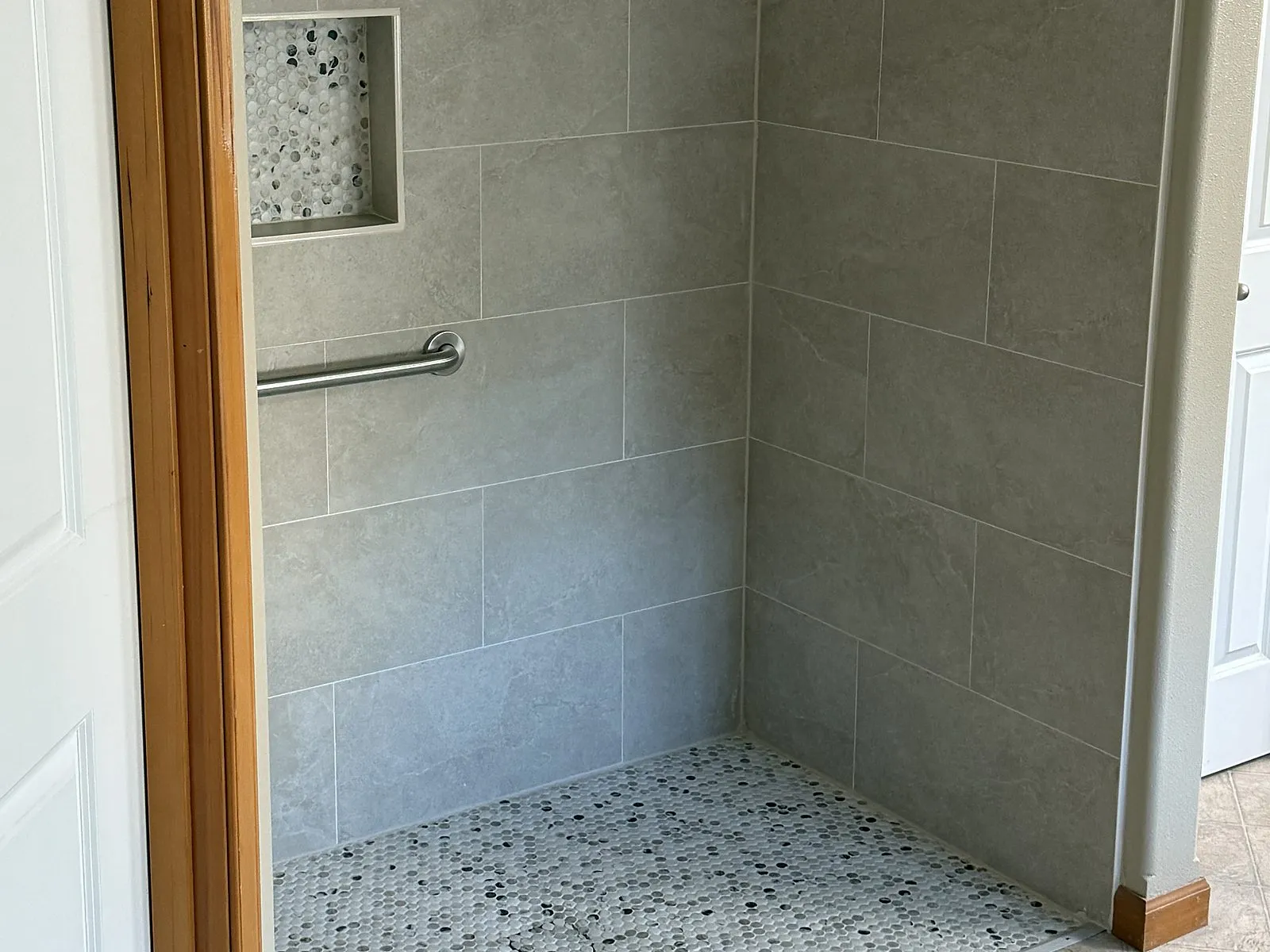 A curbless roll-in tile shower with a grab bar and pebble mosaic floor