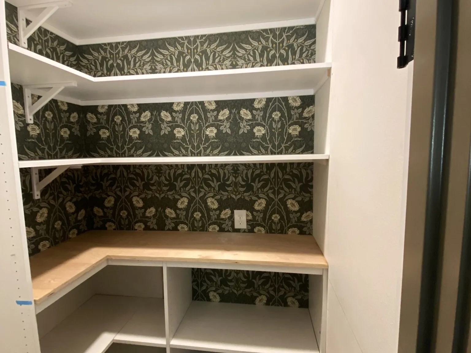 A custom built-in pantry with white shelving and patterned wallpaper
