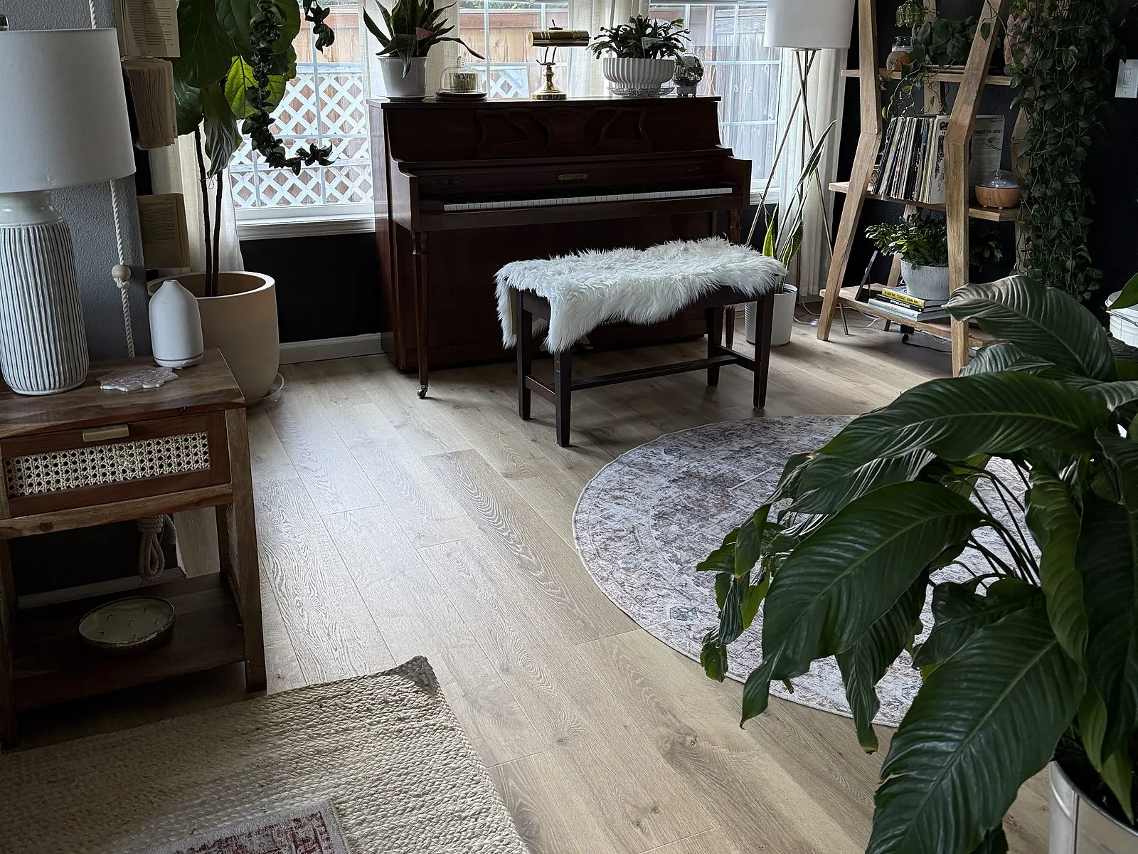 A living room with new light-toned plank flooring, a piano and houseplants