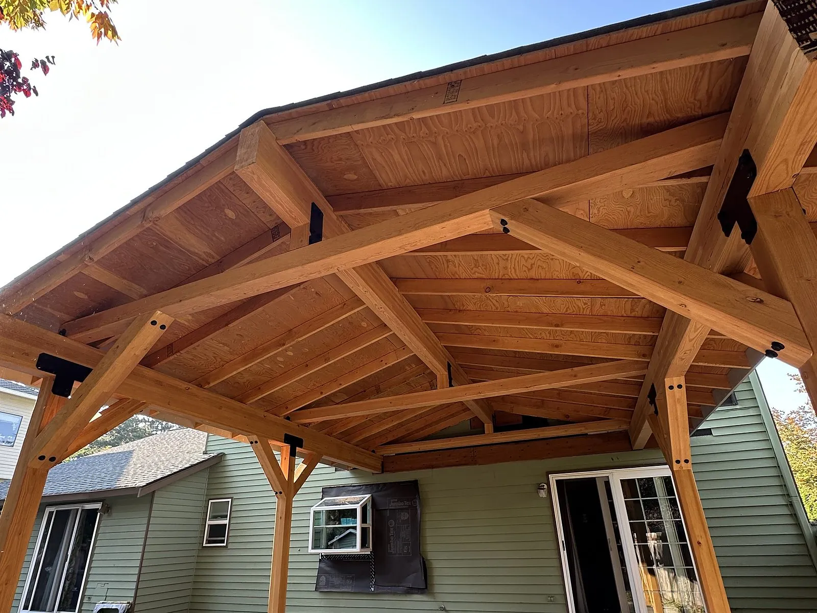 A heavy-timber pavilion with exposed rafters over a concrete patio, seen from below