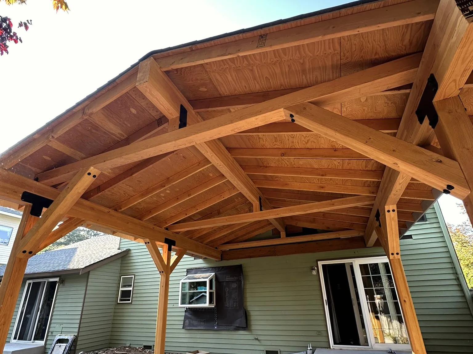 A finished cedar pergola with exposed timber trusses over a concrete patio