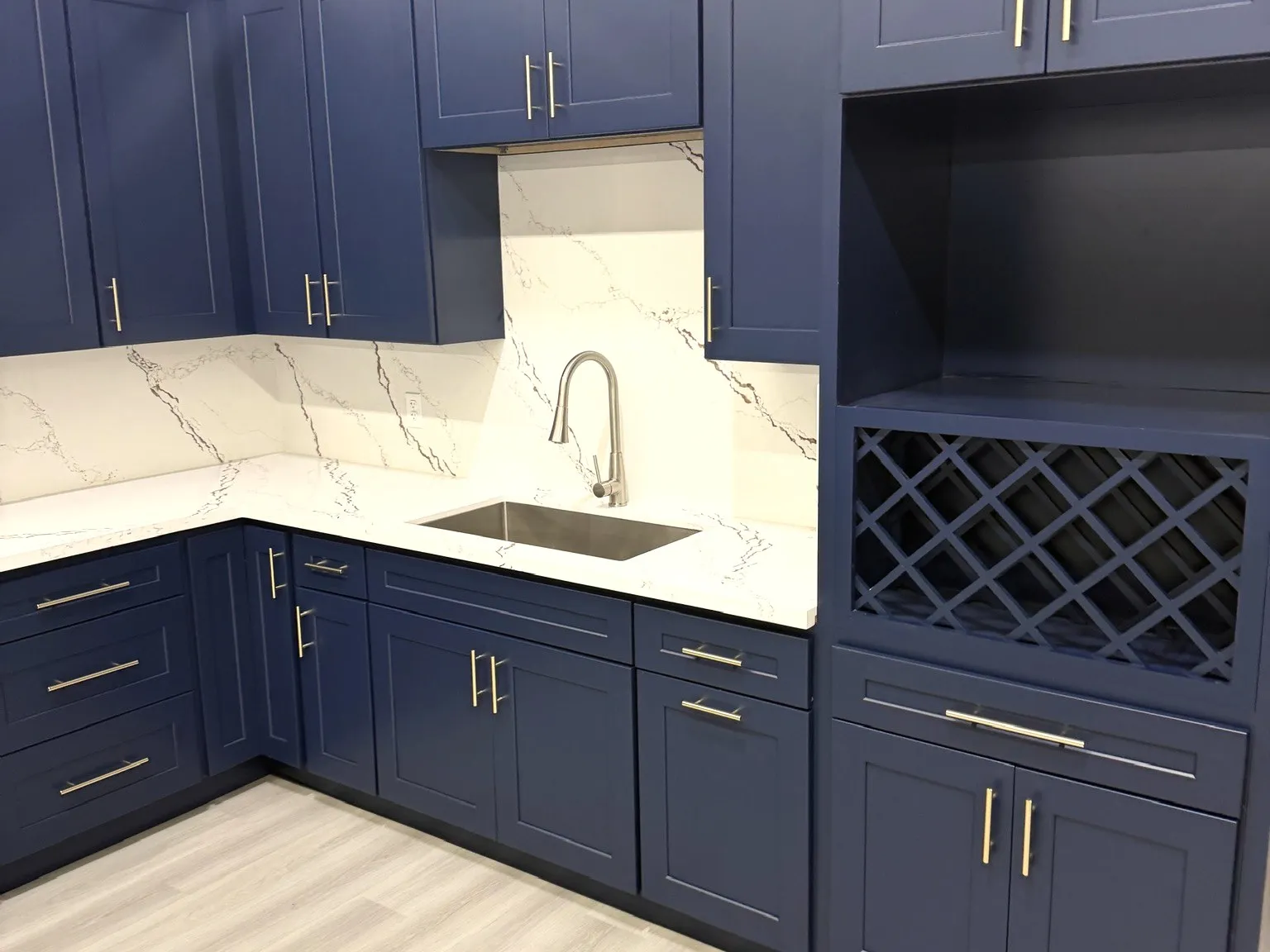 A finished kitchen with navy cabinets, marble counters and gold hardware